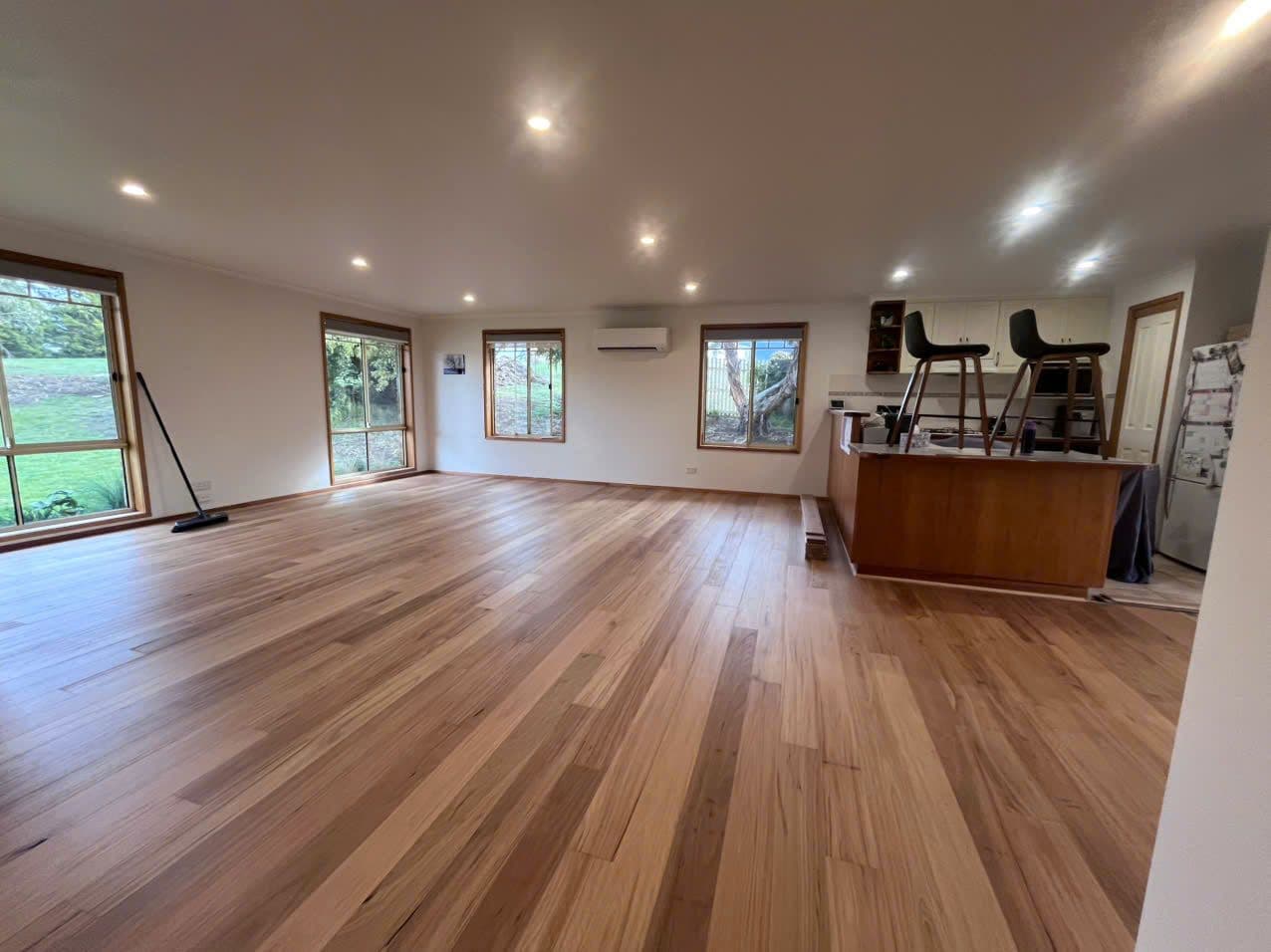Freshly laid blackbutt-toned planks across a large cottage living room, garden through every window.