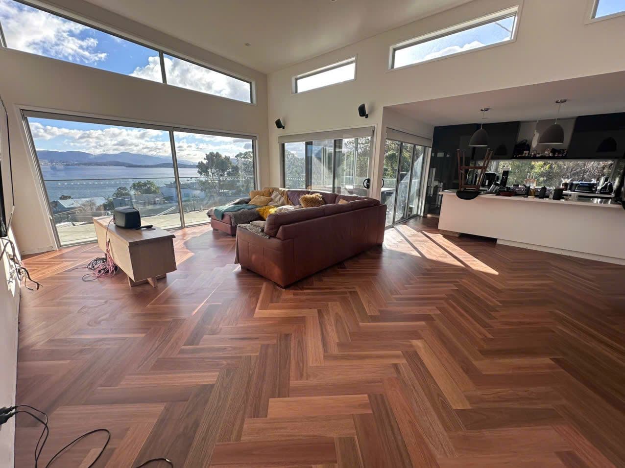 Herringbone timber floor across the living room, water views through floor-to-ceiling glass.